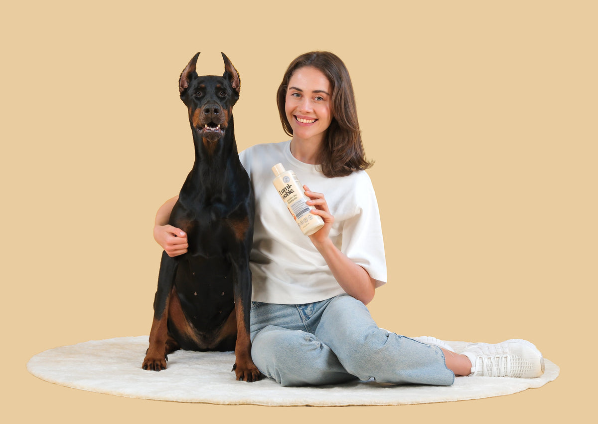 Pet parent sitting with a Doberman and holding Lumi-noble Fragrance Free Sensitive Pet Shampoo
